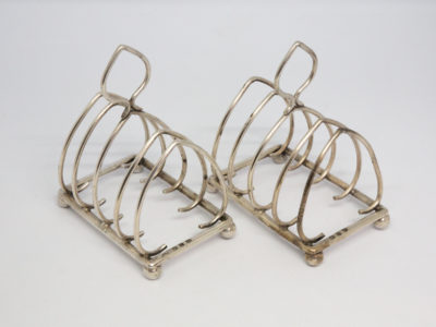 Pair of antique sterling silver toast racks. Small but sweet pair of toast racks. c1899 Birmingham assay and made by William Hutton. Each toast rack measures 72mm long, 47mm wide and 85mm tall at central point. Main photo showing both racks side by side and at a slight diagonal angle across the page.