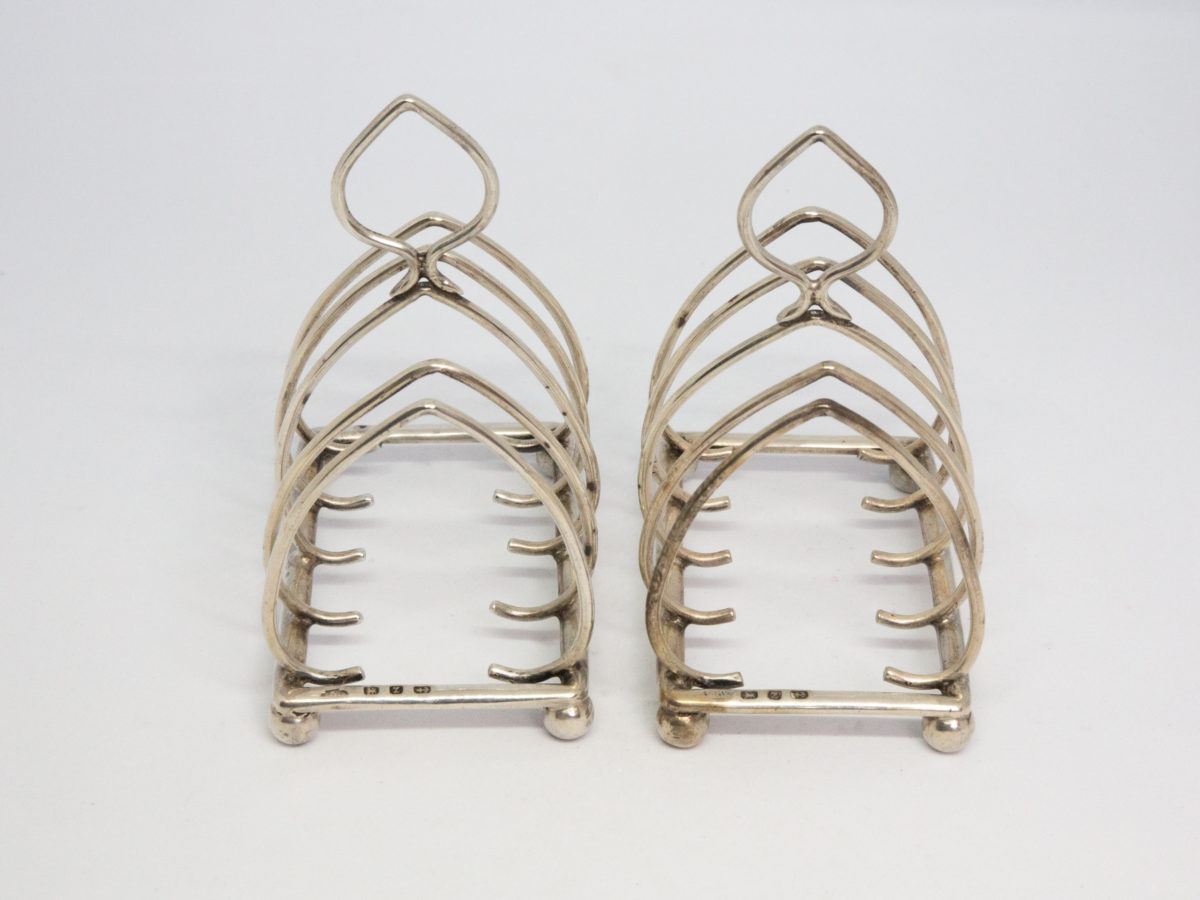 Pair of antique sterling silver toast racks. Small but sweet pair of toast racks. c1899 Birmingham assay and made by William Hutton. Each toast rack measures 72mm long, 47mm wide and 85mm tall at central point. Photo of racks side by side width ways.