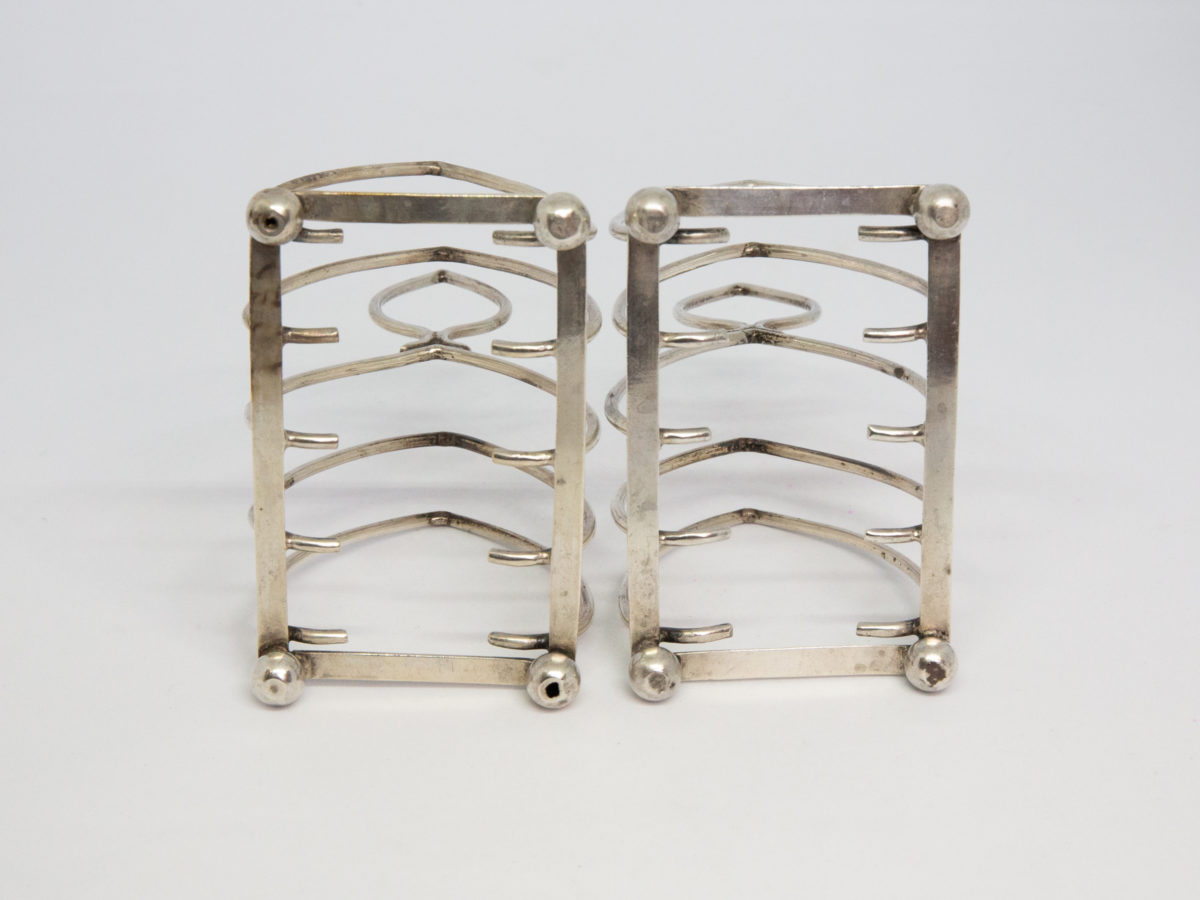 Pair of antique sterling silver toast racks. Small but sweet pair of toast racks. c1899 Birmingham assay and made by William Hutton. Each toast rack measures 72mm long, 47mm wide and 85mm tall at central point. Photo of bottom of both racks showing the ball feet.