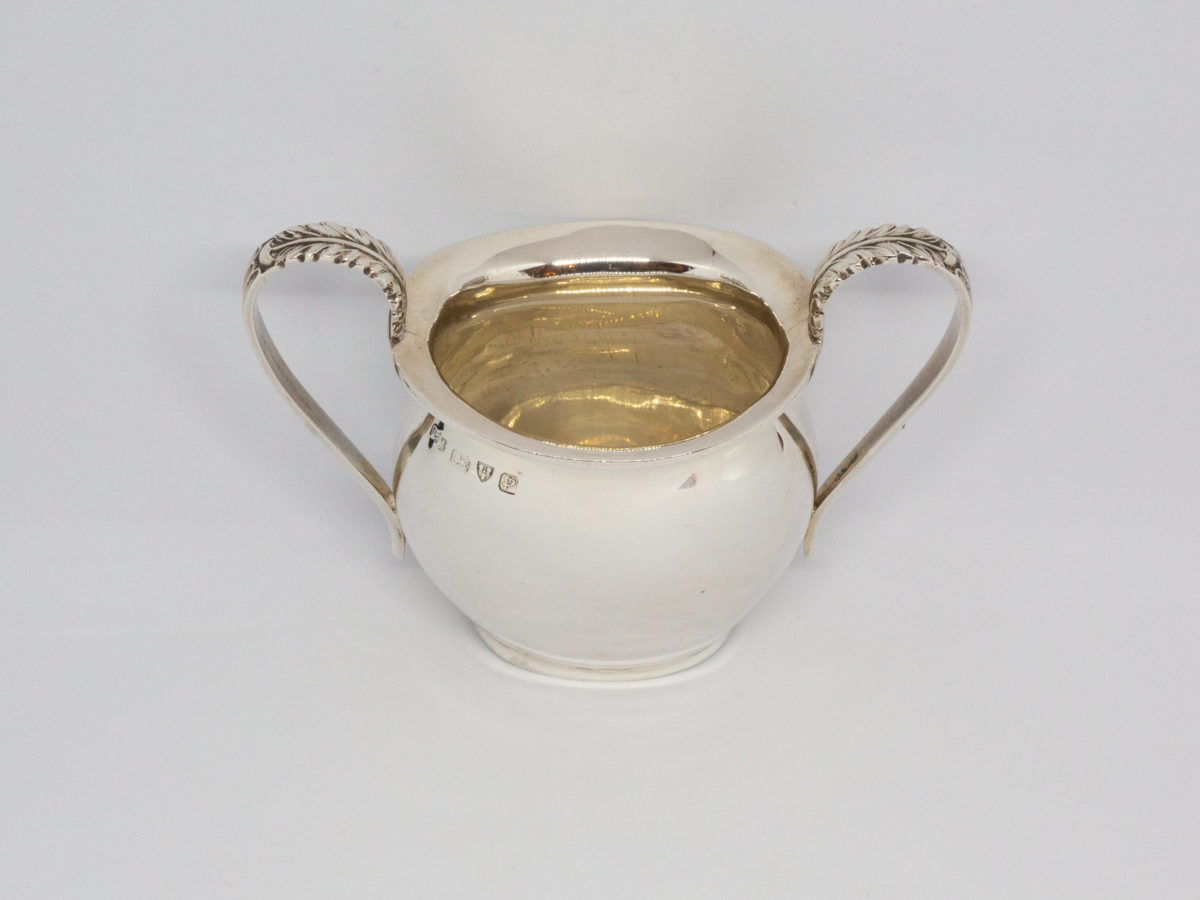 c1940 Sterling silver sugar basin. Petite sterling silver sugar basin with a plain body and classical handles with leaf design to the tops of each. Full hallmark for Chester assay to just below the rim. Measures 120mm from edge of handle to handle, 58mm across the top, base measures 46mm by 38mm, 63mm high from base to lip of basin and 85mm high from top of handle to base. Photo of basin from hallmarked side shown from slightly raised height