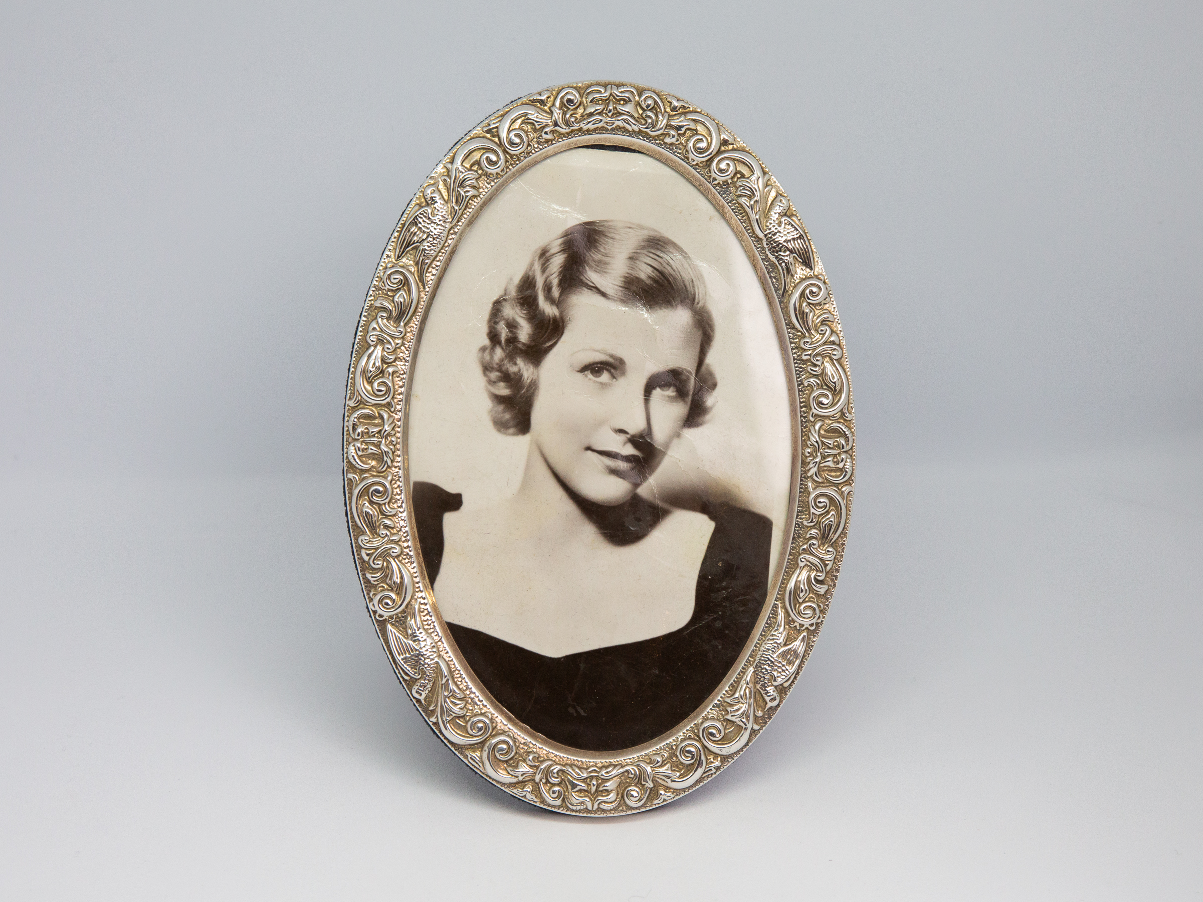 Modern oval silver photo frame. c2004 Birmingham assayed sterling silver photo frame made by WI Broadway & Co. Nice pattern work around the frame with birds. Photo area opening measures 138mm tall by 88mm at widest. Main photo of frame looing straight on.