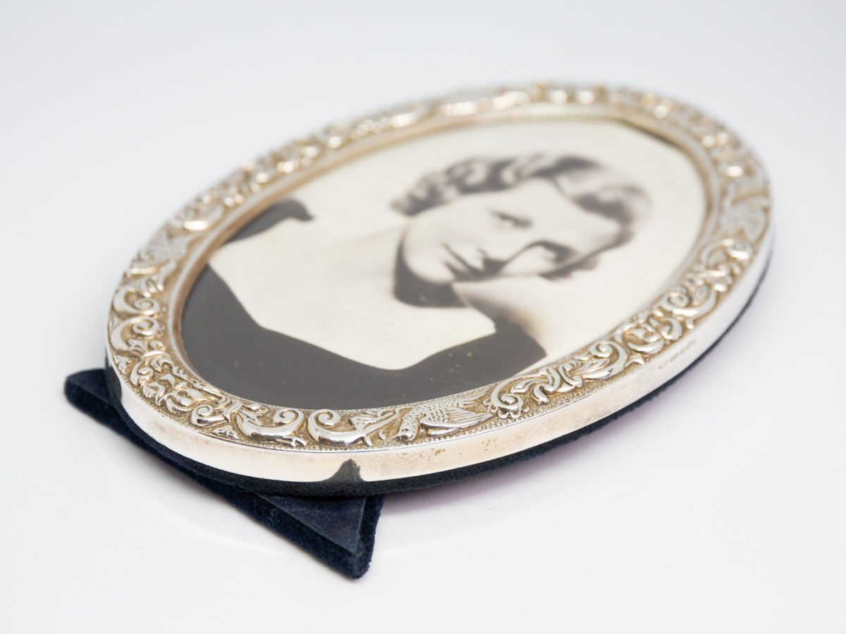 Modern oval silver photo frame. c2004 Birmingham assayed sterling silver photo frame made by WI Broadway & Co. Nice pattern work around the frame with birds. Photo area opening measures 138mm tall by 88mm at widest. Photo of frame laid flat with bottom of the frame in the bottom left corner.