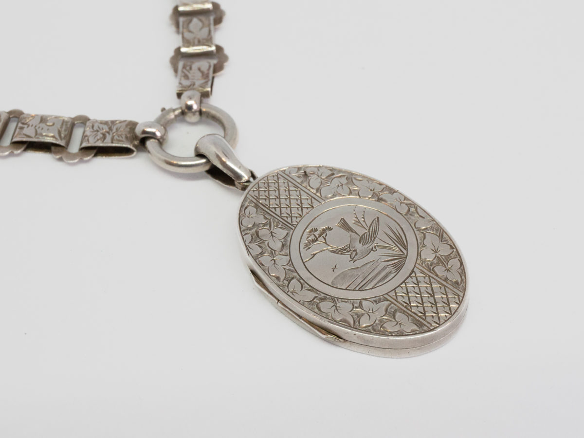 Victorian silver locket and collar. Antique sterling silver oval locket with nature themed design of bird and flora to the front on a flora themed collar chain. Full hallmark to the back of locket for Birmingham assay c1882 and Sterling Silver mark on the pendant bail. Clasp is at the front. Pendant drop length 50mm. Photo of the pendant area showing the clasp to the ring connecting pendant to chain
