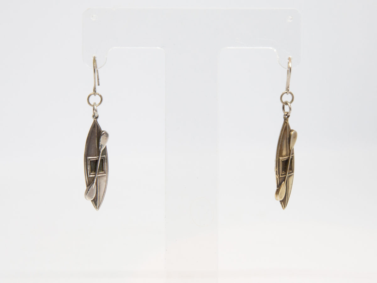 Victorian silver canoe earrings. Very unusual pair of canoe earrings with oar across the top of canoe. One canoe is silver coloured whilst other has slight golden hue and maybe gilded to distinguish 2 sides (Oxford V Cambridge perhaps?) Antique kitemark hallmark to the back of each canoe c1880. (This year being significant in that it is the only time in the history of the boat race that it was postponed for 2 days due to thick fog) Drop length approximately 45mm with canoe measuring approximately 30mm. Earrings weight 2.8gms. Box included. Photo of earrings displayed on a stand.
