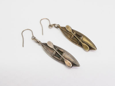 Victorian silver canoe earrings. Very unusual pair of canoe earrings with oar across the top of canoe. One canoe is silver coloured whilst other has slight golden hue and maybe gilded to distinguish 2 sides (Oxford V Cambridge perhaps?) Antique kitemark hallmark to the back of each canoe c1880. (This year being significant in that it is the only time in the history of the boat race that it was postponed for 2 days due to thick fog) Drop length approximately 45mm with canoe measuring approximately 30mm. Earrings weight 2.8gms. Box included. Main photo of earrings laid side by side on a flat surface with silver coloured one in the foreground and distinctively golden hued canoe and oar in the background.