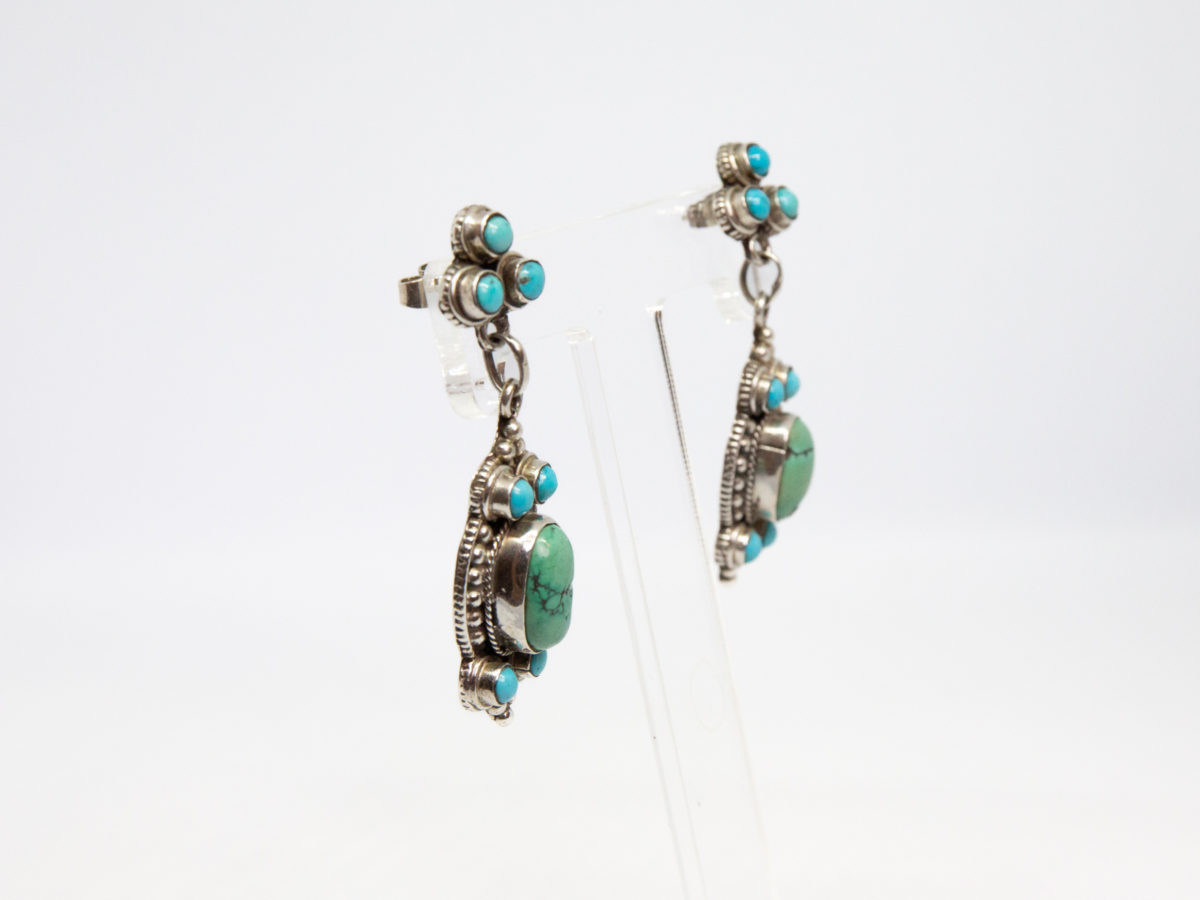 Navajo sterling silver and turquoise earrings. Lovely pair of Native American sterling silver earrings set with 2 shades of turquoise stones.Hallmarked 925 to back of both earrings and to butterfly clasps. Drop length approximately 60mm and width at widest point 18mm. Photo of earrings displayed on a stand and seen from a slight side angle.