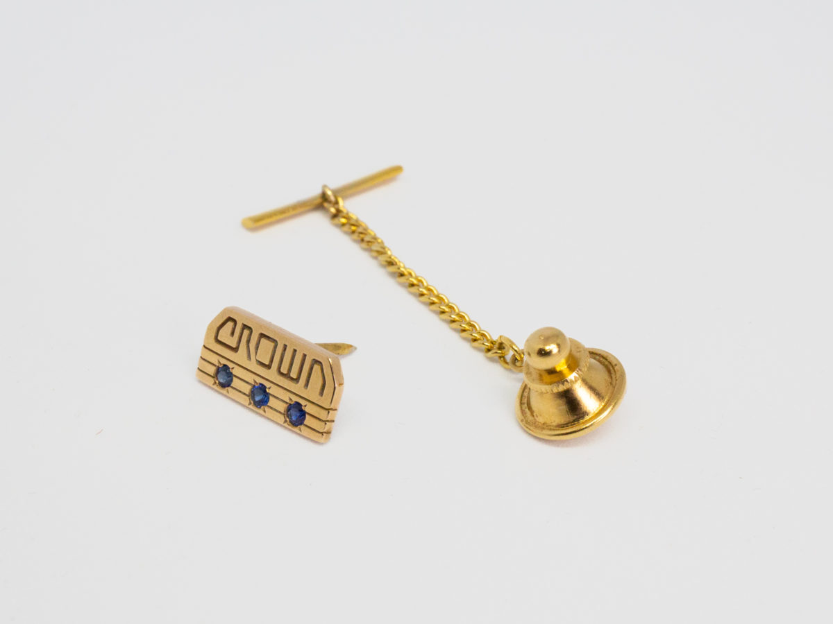 Vintage American 10 karat gold tie tack. Lovely tie tack in 10 karat gold with 3 round cut sapphires below the word crown. (Great sapphire anniversary gift perhaps?) Hallmarked 10k to the back. No hallmark to the pin guard, chain or T-bar. Tack front measures 15mm by 7mm. Photo of tie tack with pin guard & T-bar removed and tack front visible