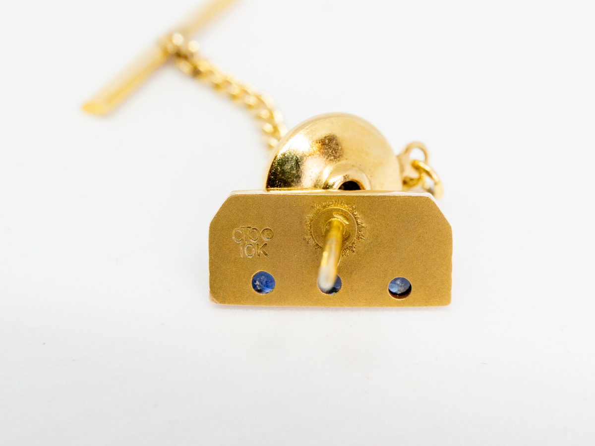 Vintage American 10 karat gold tie tack. Lovely tie tack in 10 karat gold with 3 round cut sapphires below the word crown. (Great sapphire anniversary gift perhaps?) Hallmarked 10k to the back. No hallmark to the pin guard, chain or T-bar. Tack front measures 15mm by 7mm. Photo of back of tie tack showing the 10k hallmark and CTO makers stamp.