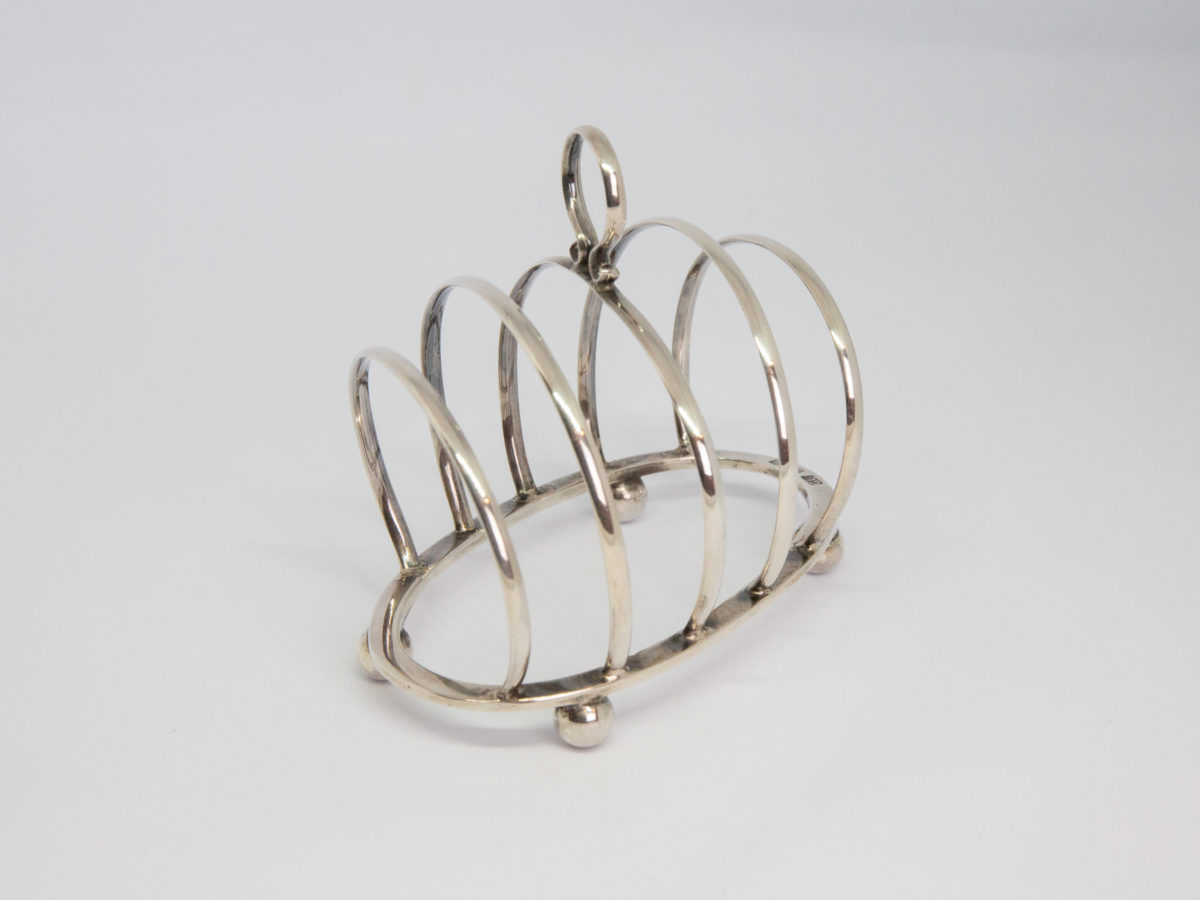 Early George V silver toast rack. Small sterling silver toast rack with partitions set at a very practical diagonal angle. Full hallmark to the top of lower frame for Birmingham assay c1919 and made by George Unite. Photo of toast rack from a slight diagonal angle.