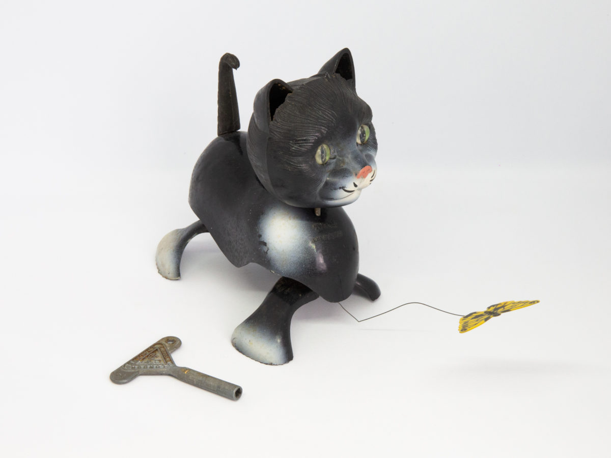 1950s Tri-Ang Minic clockwork cat. Fun novelty clockwork cat toy that chases a butterfly. Oddly realistic in detail. No original box or key. Key is included but not the original one. Cat measures approximately 100mm long, 107mm tall (at head) and 65mm wide. Main photo of cat appearing to be looking at butterfly with key in the foreground. Cat is facing bottom left of photo. Photo of cat from another angle with cat facing to bottom right of photo.