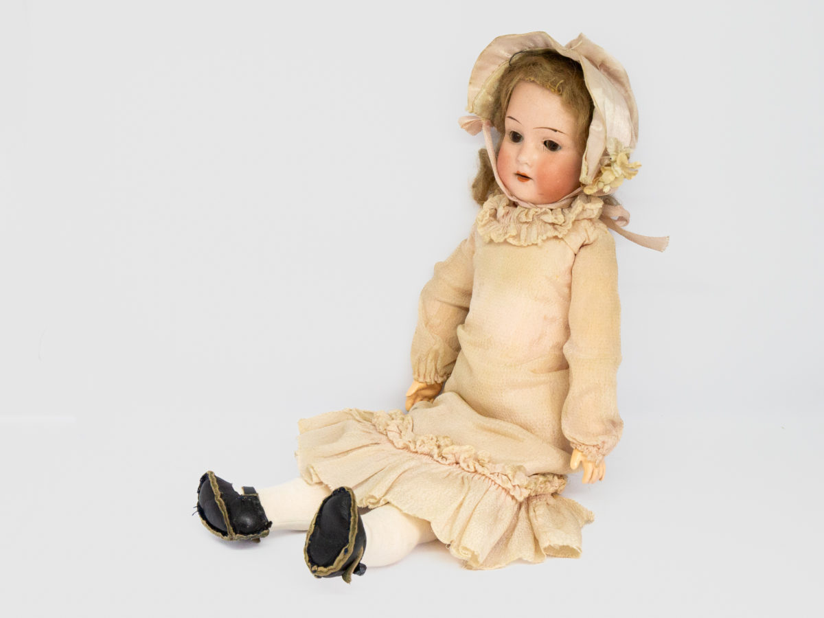 Antique Armand Marseille doll number 7. Petite bisque head doll in pale peach colour attire with incredibly realistic hand-painted features. Some wear to the clothing but otherwise in fabulous condition for a doll c1915. Measures approximately 335mm tall, 75mm wide at the hips and 55mm deep. Photo of doll seated and shown from a slight sideways angle with dolls head facing to left of photo.