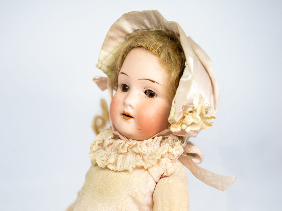 Antique Armand Marseille doll number 7. Petite bisque head doll in pale peach colour attire with incredibly realistic hand-painted features. Some wear to the clothing but otherwise in fabulous condition for a doll c1915. Measures approximately 335mm tall, 75mm wide at the hips and 55mm deep. Close up photo of the dolls hand-painted face from a slight sideways angle.