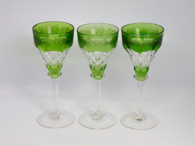 3 Art Deco cut crystal hock glasses. Lovely set of 3 hock glasses in a beautiful green to the top & bottom rims and a faceted detail to the centre of glass bowl. Etched vine design in the top green rim and clear stems and bases. Made by John Walsh. Each glass measures approximately 60mm in diameter at base and top and 150mm tall. Weight varies slightly with each glass with lightest at 123gms and heaviest at 152gms. Main photo of all three glasses lined up in a line taken from a near eye level.