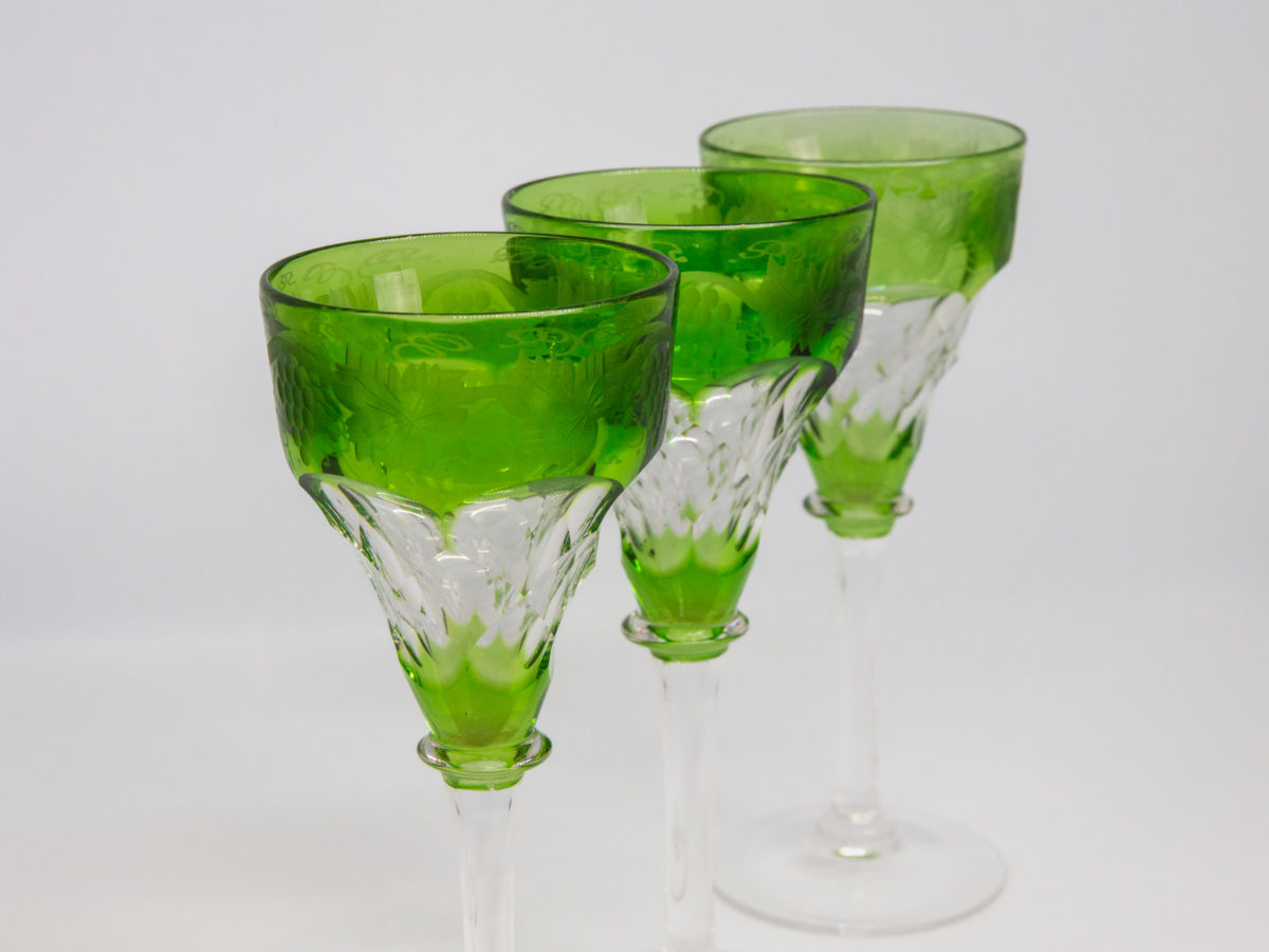 3 Art Deco cut crystal hock glasses. Lovely set of 3 hock glasses in a beautiful green to the top & bottom rims and a faceted detail to the centre of glass bowl. Etched vine design in the top green rim and clear stems and bases. Made by John Walsh. Each glass measures approximately 60mm in diameter at base and top and 150mm tall. Weight varies slightly with each glass with lightest at 123gms and heaviest at 152gms. Photo of 3 glasses shown diagonally in a row.