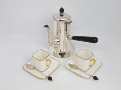 c1907 Small silver coffee pot with cups. Fabulous coffee set consisting of a small antique sterling silver coffee pot with ebony finial and handle, and a pair of small square white porcelain cups & saucers. The cups and saucers are accentuated with gold on the handles & rims and to finish the set is a pair of small sterling silver coffee spoons with ebony coffee bean to the tip of each handle. Each piece of silver is hallmarked for Birmingham assay and made by Heath & Middleton with additional retailers stamp to base of coffee pot for Albert Barker Ltd, New Bond St, London. The coffee pot measures 92mm in diameter at base165mm at widest at handle, 155mm at tallest by finial and weighs 274.2gms. Cups measure 30mm square at base, 55mm at widest at handle, 40mm square at top and 48mm high. Spoons measure 95mm long. Main photo showing all items displayed together with coffee pot in background and the 2 coffee cups, saucers & spoons in foreground.