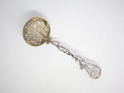 c1853 Sterling silver fruit strainer spoon. Very fine quality & beautifully crafted sterling silver fruit strainer spoon in a vine pattern. The handle is made to resemble vine stalks and leaves with an extended vine leaf design for the spoon bowl which is finished in gilt. Full hallmark to the top vine leaf for Birmingham assay and made by Hilliard & Thomason. Spoon bowl measures 45mm by 40mm. Main photo of spoon on a flat surface and looking directly down from above. Spoon bowl is to the top left corner of photo