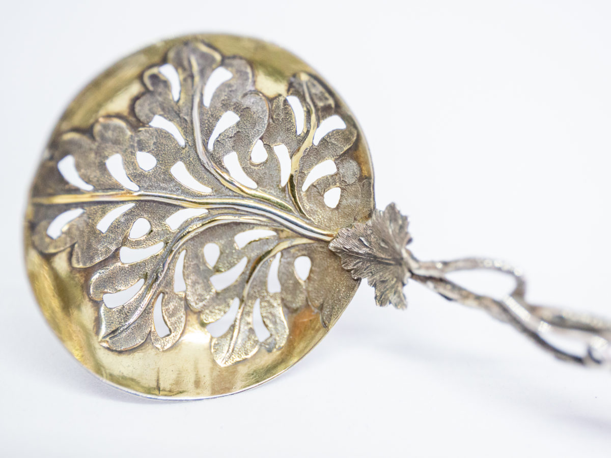 c1853 Sterling silver fruit strainer spoon. Very fine quality & beautifully crafted sterling silver fruit strainer spoon in a vine pattern. The handle is made to resemble vine stalks and leaves with an extended vine leaf design for the spoon bowl which is finished in gilt. Full hallmark to the top vine leaf for Birmingham assay and made by Hilliard & Thomason. Spoon bowl measures 45mm by 40mm. Close up photo of inside of spoon bowl showing the gilt work with some gilt wear visible.