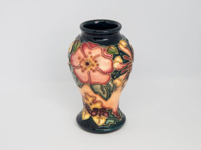 Moorcroft Oberon honeysuckle vase. Small Moorcroft vase in classic Moorcroft colours and decorated in the Oberon honeysuckle pattern. Markings to the base are faded but still just readable. Designed by Rachel Bishop and dated c1993. Measures 46mm in diameter at base, 57mm at widest point and 34mm across the top. Main photo showing dog rose in bloom with part of honeysuckle flower to the right and violets at the bottom.