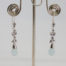Modern 18 karat white gold, aquamarine and sapphire earrings. Sophisticated & sweet dangle earrings in 18 karat white gold set with small round cut sapphires and a droplet of carved aquamarine to finish off at the ends. Earring drop length approximately 50mm from top of hook to bottom of aquamarine droplet. Main photo showing both earrings hanging displayed on a stand.