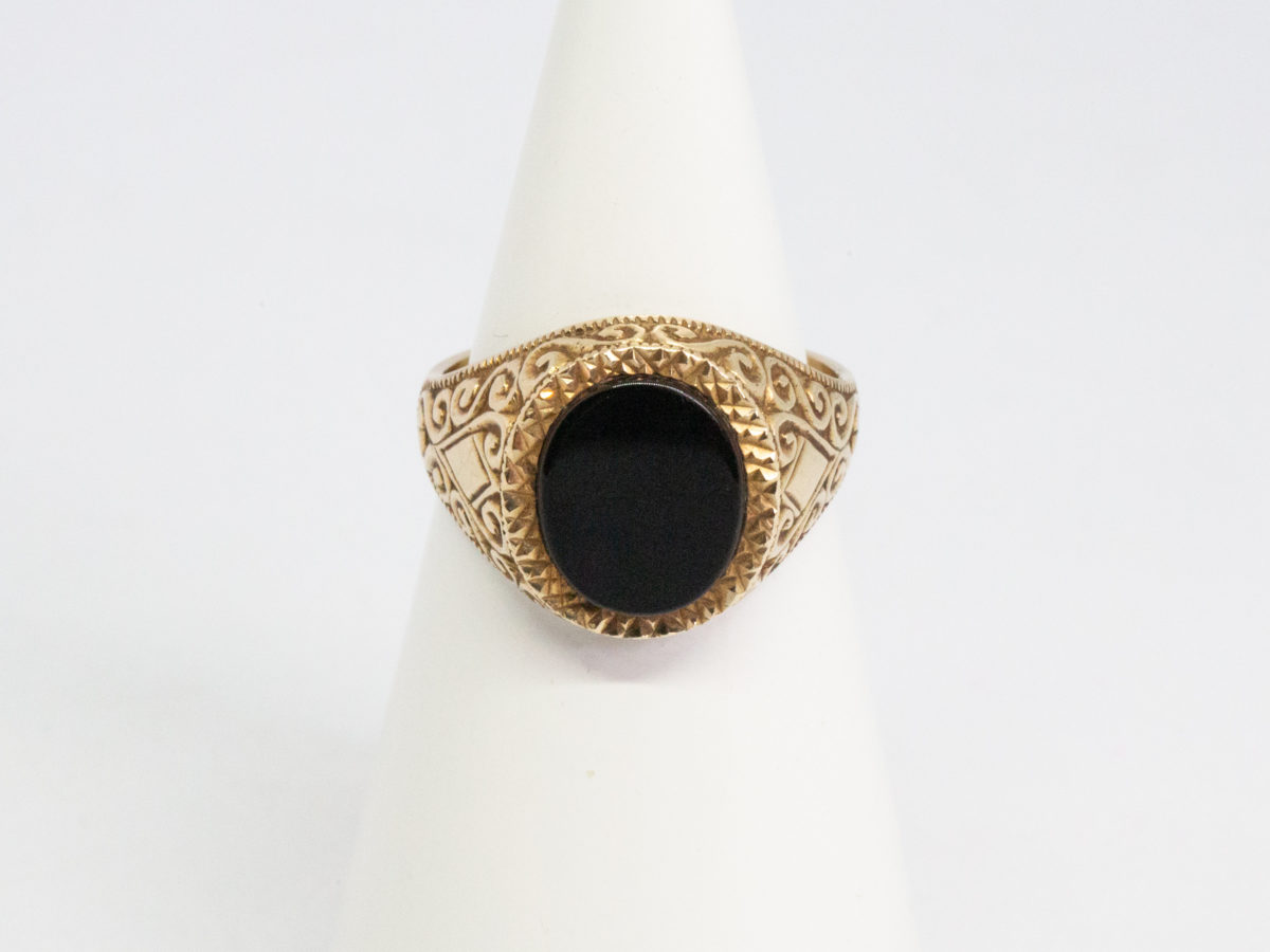 Vintage 9 karat gold and black onyx ring. Smooth oval black onyx to the centre of fine cut mini pyramid frame with fancy scrollwork to each shoulder. Fully hallmarked for Continental import and assayed in Birmingham. Ring size R.5 / 9. Main photo showing ring displayed on a cone shaped stand and seen from the ring front straight on.