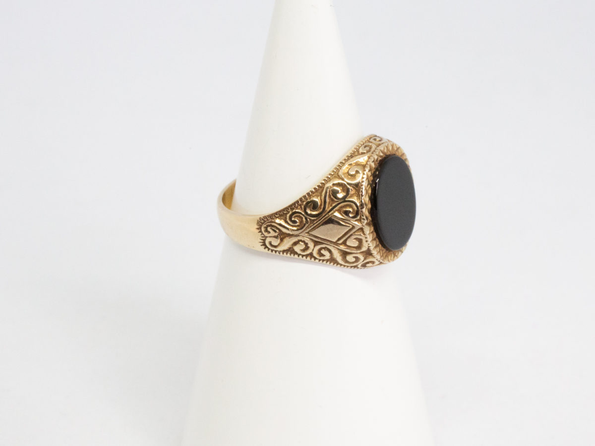 Vintage 9 karat gold and black onyx ring. Smooth oval black onyx to the centre of fine cut mini pyramid frame with fancy scrollwork to each shoulder. Fully hallmarked for Continental import and assayed in Birmingham. Ring size R.5 / 9. Photo of ring displayed on a cone shaped display stand with ring front facing right of photo.
