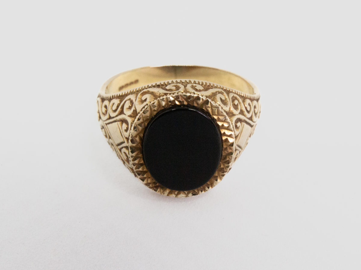 Vintage 9 karat gold and black onyx ring. Smooth oval black onyx to the centre of fine cut mini pyramid frame with fancy scrollwork to each shoulder. Fully hallmarked for Continental import and assayed in Birmingham. Ring size R.5 / 9. Photo of ring on a flat surface and seen front on.