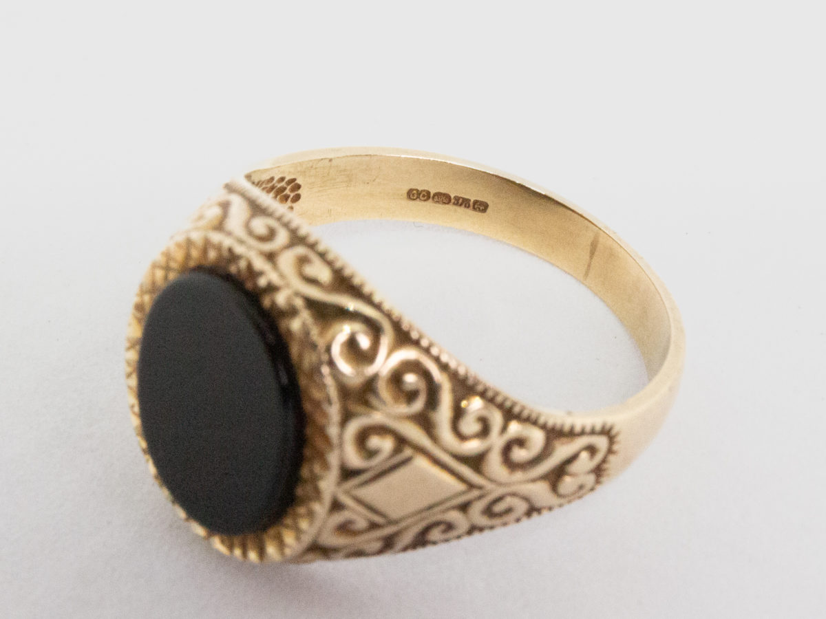 Vintage 9 karat gold and black onyx ring. Smooth oval black onyx to the centre of fine cut mini pyramid frame with fancy scrollwork to each shoulder. Fully hallmarked for Continental import and assayed in Birmingham. Ring size R.5 / 9. Photo revealing the full hallmark on the inside band of ring.