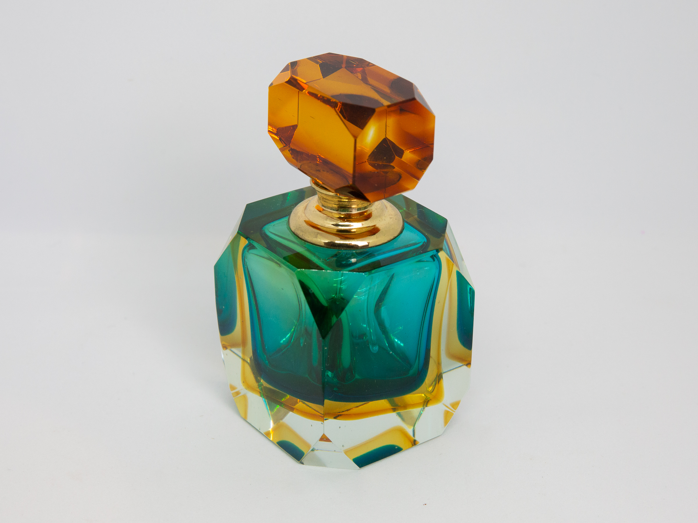 Mid century modern Murano glass perfume bottle. Small stunning Murano Sommerso perfume bottle in burnt amber, aqua and clear glass. Screw top stopper with brass neck and clear glass applicator. A really beautiful piece of modern glass art attributed to Flavio Poli. Main photo of bottle set at a slight angle with one corner edge to the centre foreground. The different colours from the Sommerso technique very visible.