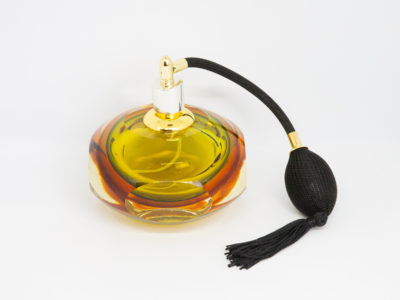 Mid century modern perfume atomiser by Murano. A beautiful piece of Sommerso glass art in shades of clear amber and pale green with a brass top and long spray atomiser in black. Interesting shape with 4 sides giving a look akin to squashed bubble. Measures 52mm in diameter at base and 105mm at bulbous central area. Main photo showing perfume atomiser bottle from a slightly raised eye level with the black spray atomiser to the right of bottle.