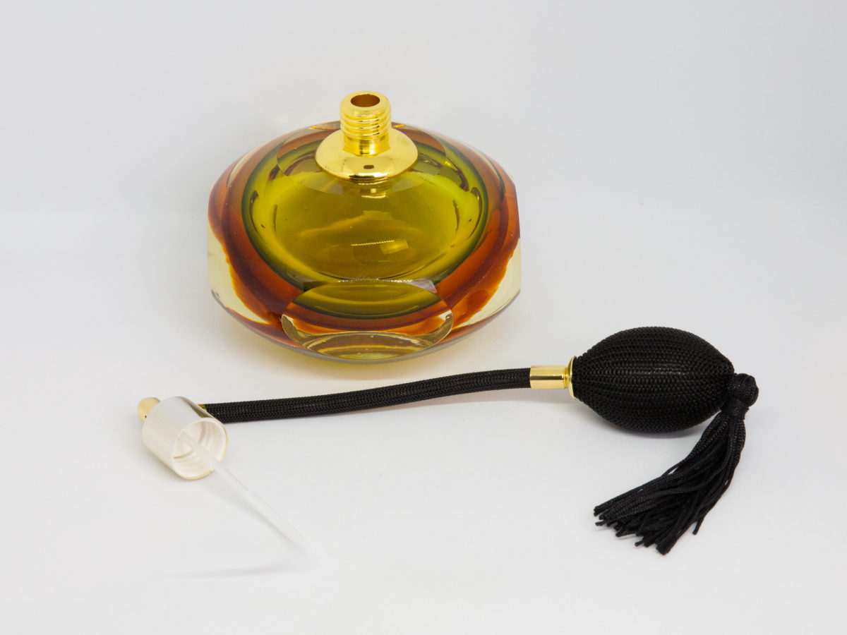Mid century modern perfume atomiser by Murano. A beautiful piece of Sommerso glass art in shades of clear amber and pale green with a brass top and long spray atomiser in black. Interesting shape with 4 sides giving a look akin to squashed bubble. Measures 52mm in diameter at base and 105mm at bulbous central area. Photo of bottle with spray atomiser removed and placed in the foreground.