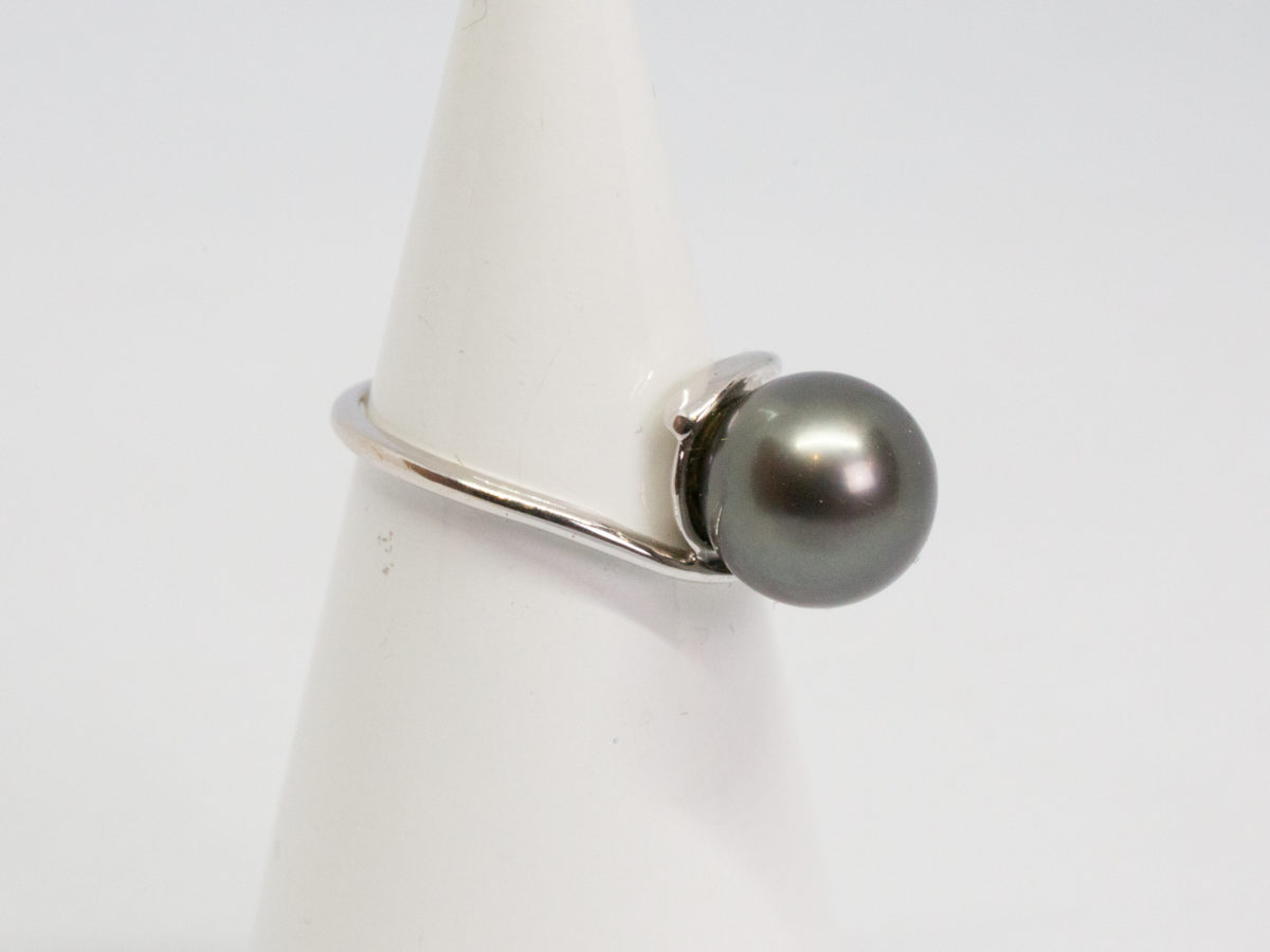 Modern Tahitian black pearl and white gold ring. Elegant and aesthetically pleasing ring in 18 karat white gold with large natural Tahitian black pearl. Comes with small ring box. Ring size N / 6.5 Ring weight 4gms. Photo of ring displayed on a cone stand and seen with pearl facing right of photo.