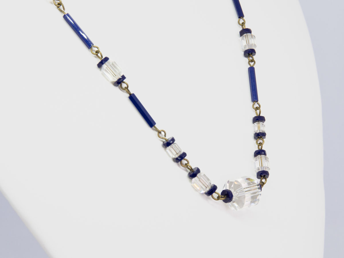 Vintage Art Deco crystal glass necklace. Subtly sparkly handmade clear and navy crystal bead necklace linked with brass throughout. c1930. Clasp not original. Close up photo of the front end of necklace shown from a side angle.