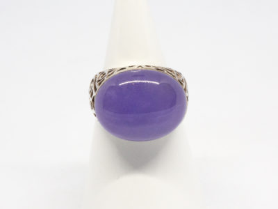 Modern sterling silver and lilac jade ring. Lovely ring with a large oval lilac jade stone set widthways to fit across the finger . Intricate scrollwork design to the silver on shoulders, gallery and bridge, Stone/ring front measures approximately 20mm by 15mm. Ring size R / 8.5. Ring weight 8.1gms. Main photo of ring on a cone shaped display stand with ring front forward facing.