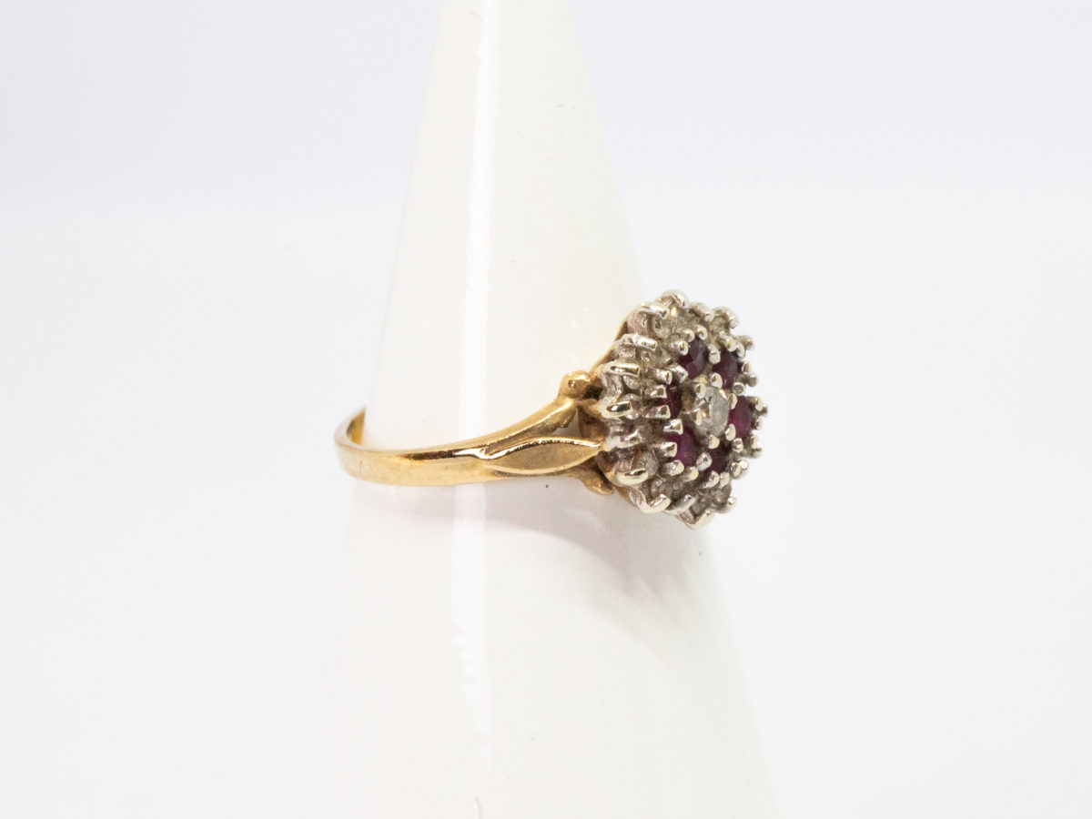 Vintage 9 karat gold ring. Pretty ring with a floral front of rubies and diamonds. Full hallmark to inside band for Birmingham assay c1987 Ring size L / 5.5. Photo of ring on a cone shaped display stand with ring front facing right.