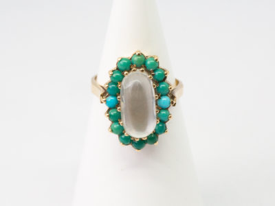 Vintage 9 karat gold ring with moonstone and turquoise. A truly stunning ring set with an oval rainbow moonstone to the centre and framed by small sleeping beauty turquoise stones. Hallmark is worn but readable for London assay. Ring front measures 20mm by 15mm. Ring size Q / 8 and weight 4.1gms. Box included. Main photo of ring on a cone shaped display stand with ring front facing forward.