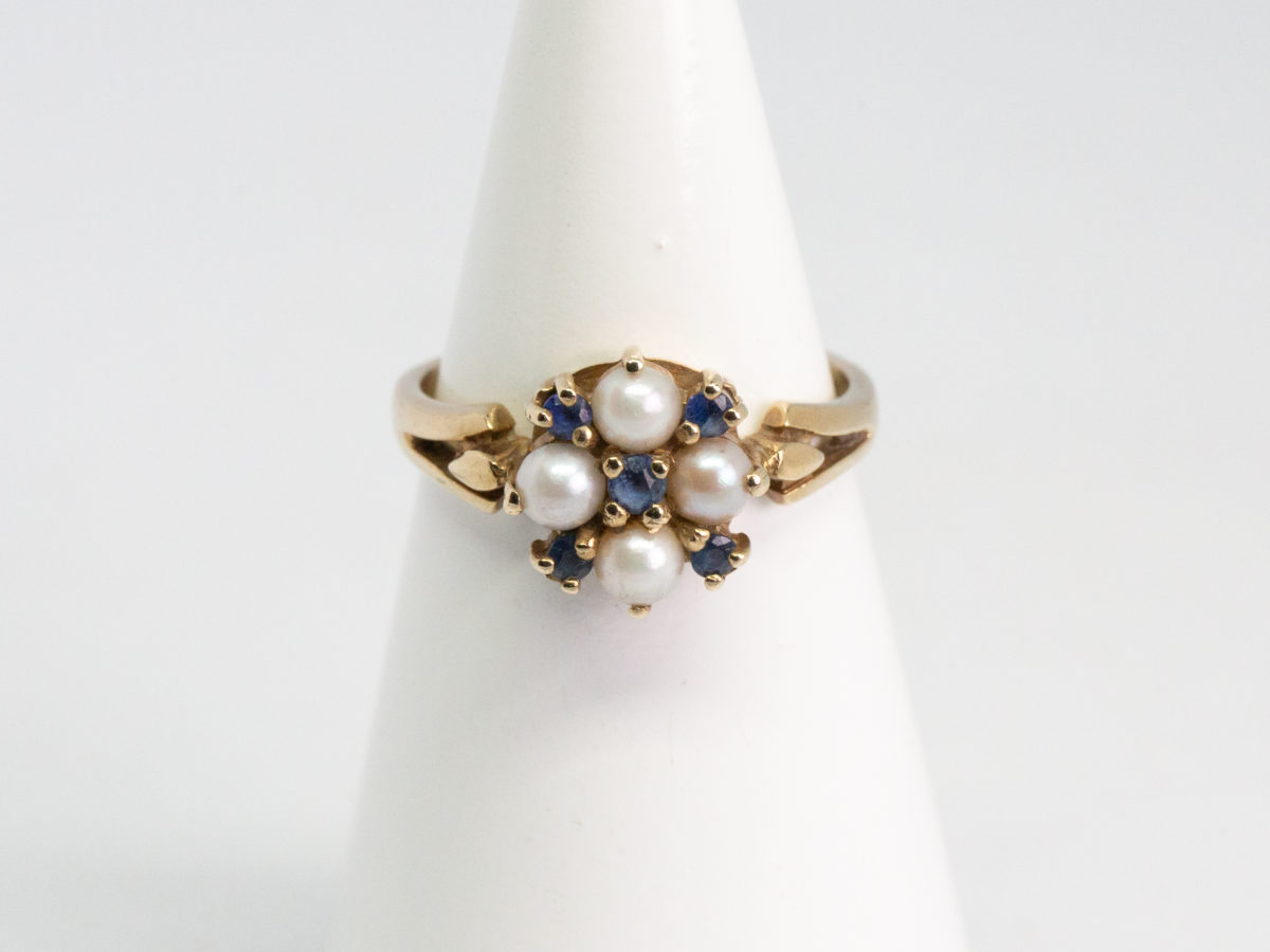 Vintage 9 karat gold, sapphire and pearl ring. Pretty 9 karat gold ring set with 5 small round cut blue sapphires and seed pearls. Hallmarked for Continental import with Birmingham assay. Ring size Q / 8. Ring weight 3.2gms. Main photo of ring displayed on a cone shaped stand with ring front facing forward.