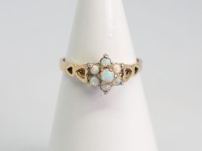 Vintage 9 karat gold and opal ring. Sweet 9 karat gold ring set with 7 small round opal stones in a flower shape with largest stone to the centre. Hallmarked 375 for 9 karat gold. Ring size O.5 / 7.25. Ring weight 2gms. Main photo of ring displayed on a cone shaped stand with ring front facing forward.