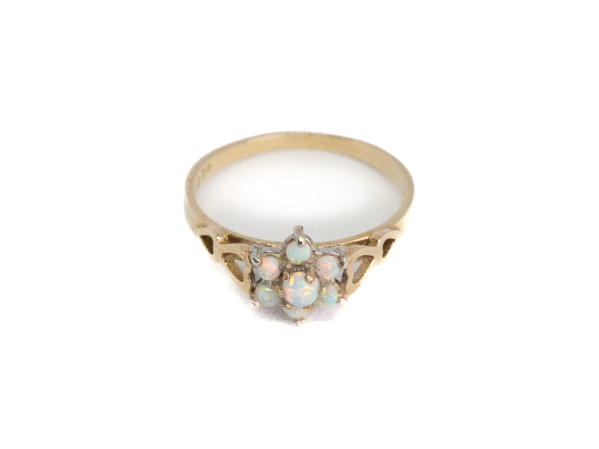 Vintage 9 karat gold and opal ring. Sweet 9 karat gold ring set with 7 small round opal stones in a flower shape with largest stone to the centre. Hallmarked 375 for 9 karat gold. Ring size O.5 / 7.25. Ring weight 2gms. Photo of ring on a flat surface with ring front facing forward.