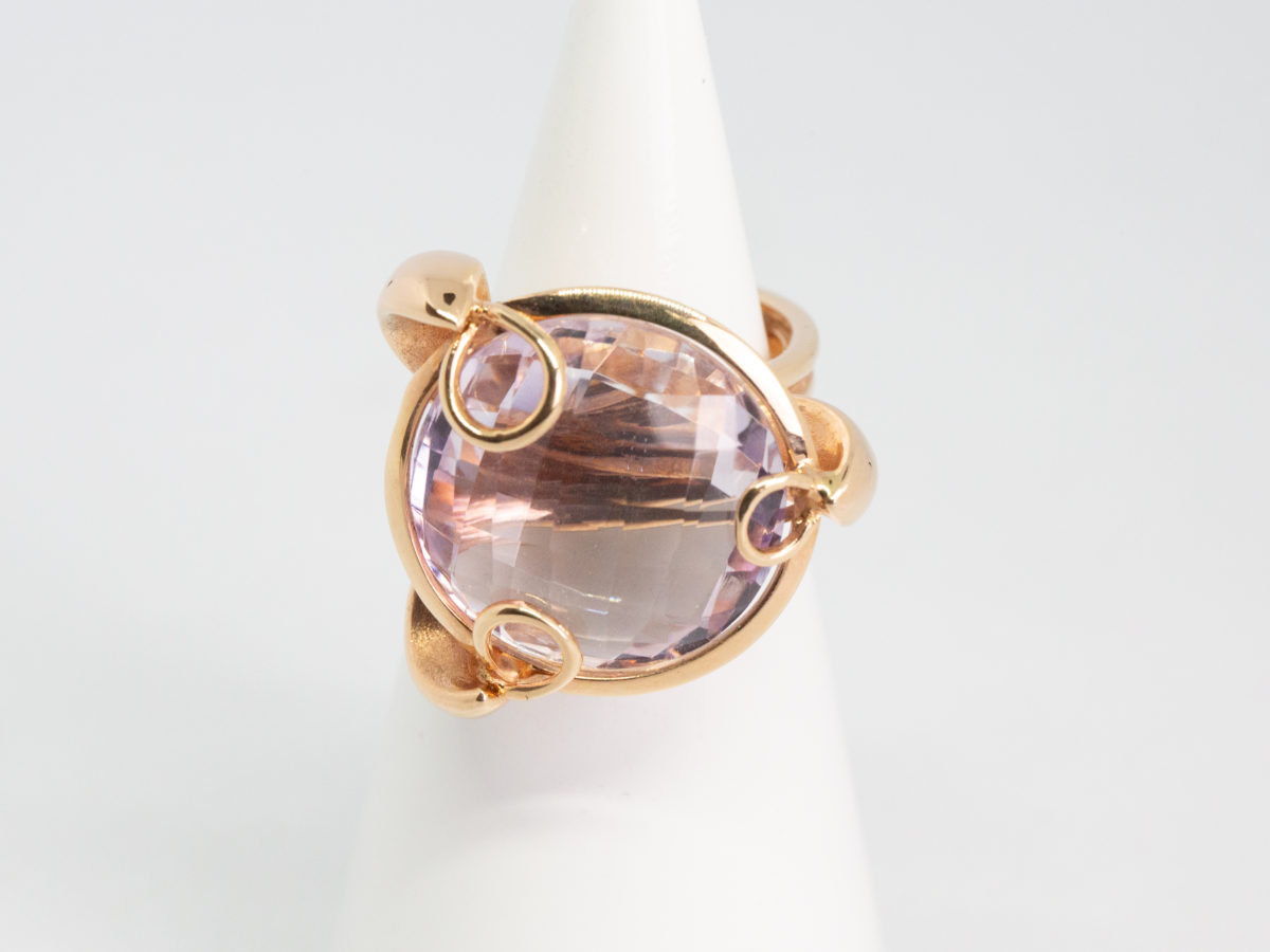 18 karat rose gold and amethyst ring. A stunning statement ring in 18 karat rose gold with a large faceted round cut lilac amethyst stone. Unusual raised setting with 3 hoop claws to secure the stone. Looks incredible worn! Italian made quality design. Hallmarked to the inside band. Ring size M / 6. Weight 12.7gms. Main photo of ring displayed on a cone shaped stand with ring front facing forward.