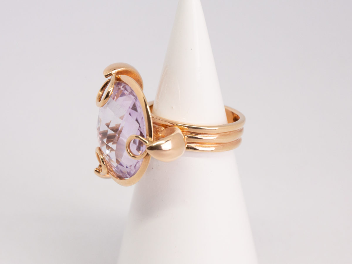 18 karat rose gold and amethyst ring. A stunning statement ring in 18 karat rose gold with a large faceted round cut lilac amethyst stone. Unusual raised setting with 3 hoop claws to secure the stone. Looks incredible worn! Italian made quality design. Hallmarked to the inside band. Ring size M / 6. Weight 12.7gms. Photo of ring on a cone shaped stand and seen with ring front facing left of photo.
