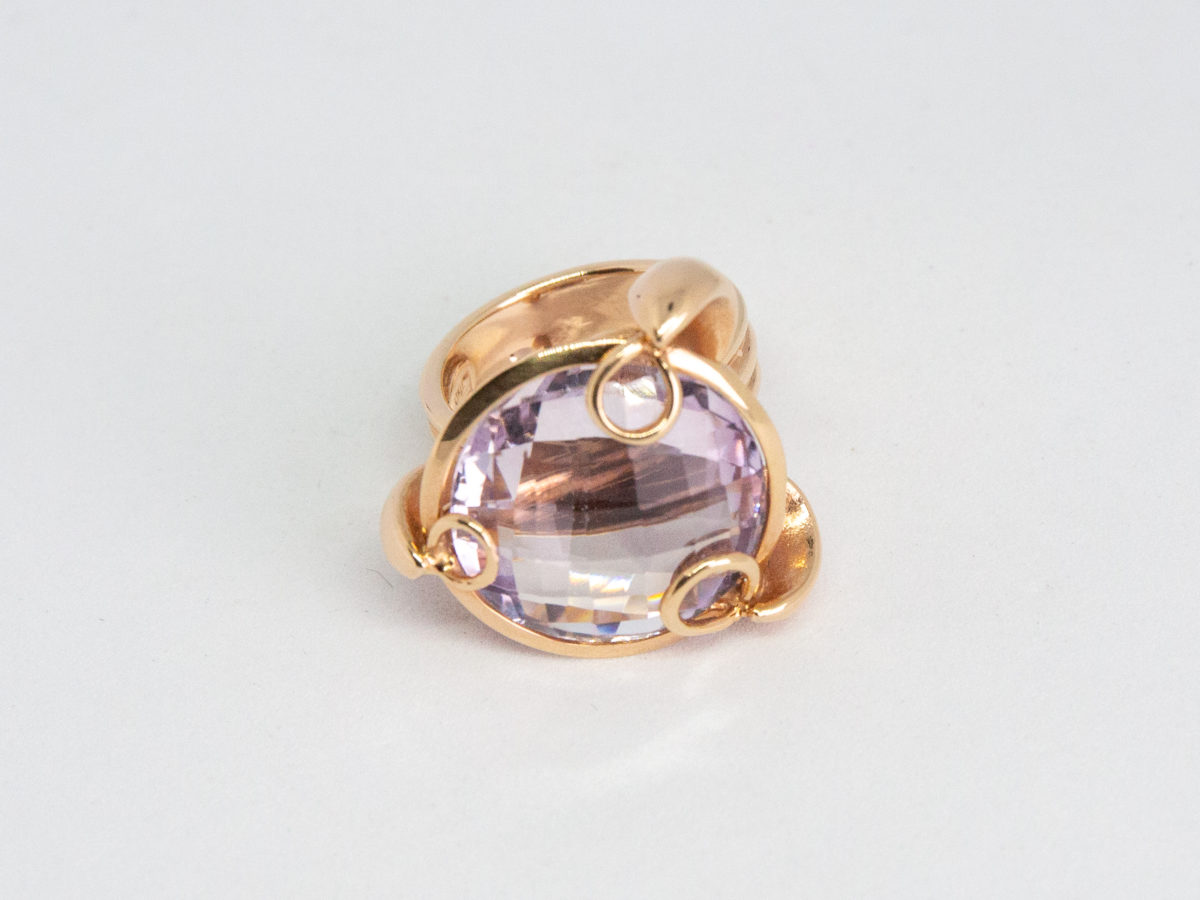 18 karat rose gold and amethyst ring. A stunning statement ring in 18 karat rose gold with a large faceted round cut lilac amethyst stone. Unusual raised setting with 3 hoop claws to secure the stone. Looks incredible worn! Italian made quality design. Hallmarked to the inside band. Ring size M / 6. Weight 12.7gms. Photo of ring on a flat surface and seen with ring front facing forward.