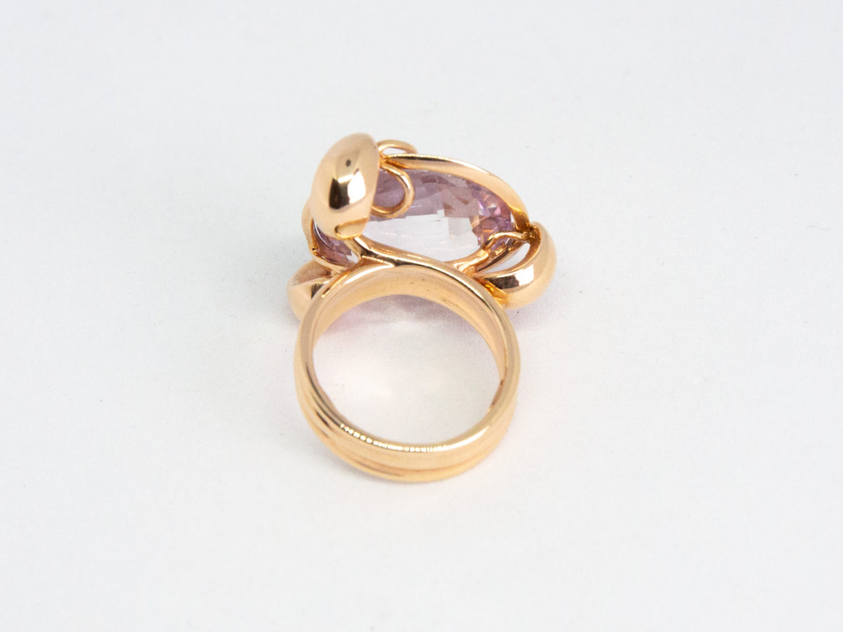 18 karat rose gold and amethyst ring. A stunning statement ring in 18 karat rose gold with a large faceted round cut lilac amethyst stone. Unusual raised setting with 3 hoop claws to secure the stone. Looks incredible worn! Italian made quality design. Hallmarked to the inside band. Ring size M / 6. Weight 12.7gms. Photo of ring on a flat surface and seen with the back of ring in the foreground.