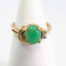 9 karat gold jade and diamond ring. Pretty 9 karat gold ring set with an apple green jade to the centre with 2 small round cut diamonds to one side & 2 gold wave curls to the other side. Hallmarked 375 to inside band. Ring size M.5 / 6.5. Weight 3.2gm. Main photo of ring displayed on a cone shaped stand and seen with ring front facing.