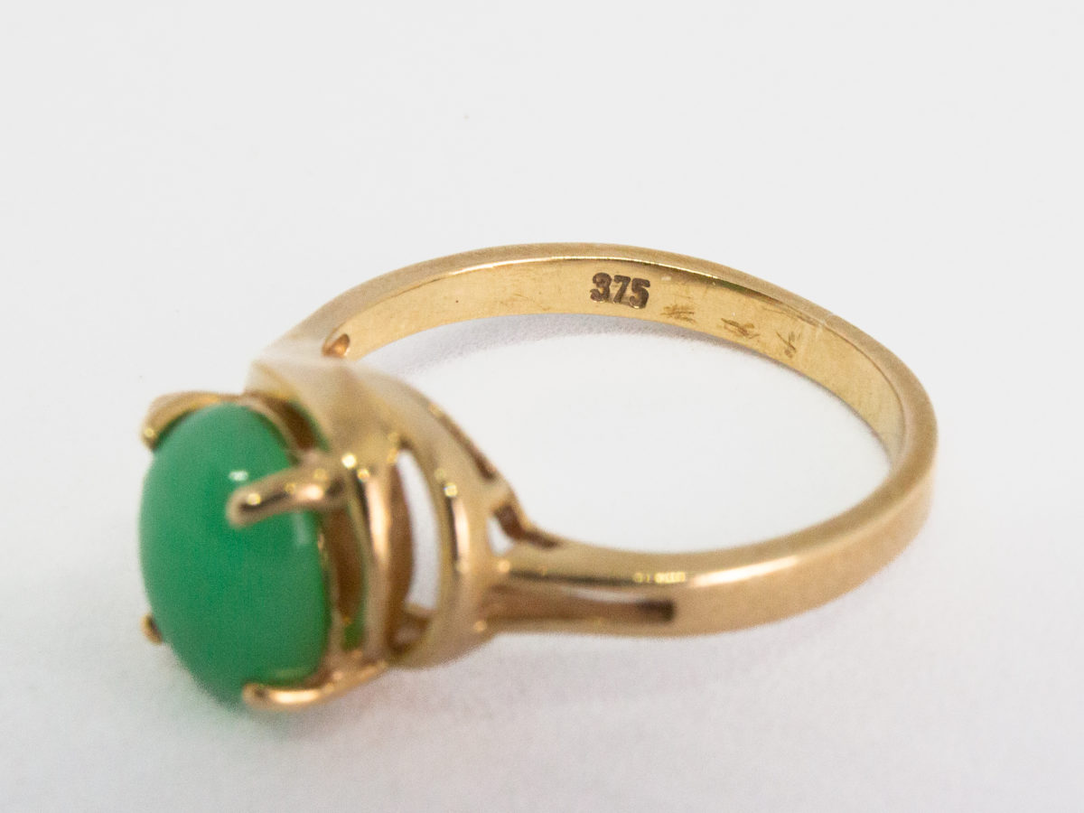 9 karat gold jade and diamond ring. Pretty 9 karat gold ring set with an apple green jade to the centre with 2 small round cut diamonds to one side & 2 gold wave curls to the other side. Hallmarked 375 to inside band. Ring size M.5 / 6.5. Weight 3.2gm. Close up photo of the 375 hallmark on the inside band.