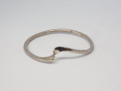 Modern sterling silver snakeskin bangle. Unusual bangle with snakeskin like pattern and a flat twist on one area giving a double snake like appearance. Fully hallmarked for London assay c2015. Inside diameter measures 65mm. Main photo of bangle on a flat surface with the 'Snake head and tail' in the foreground.