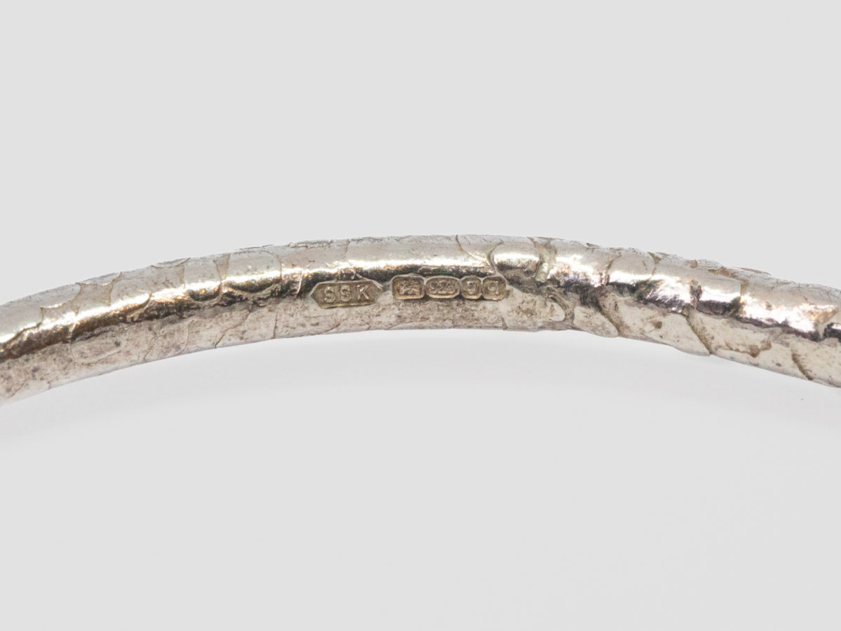 Modern sterling silver snakeskin bangle. Unusual bangle with snakeskin like pattern and a flat twist on one area giving a double snake like appearance. Fully hallmarked for London assay c2015. Inside diameter measures 65mm. Close up photo of the full hallmark to the inside of bangle.