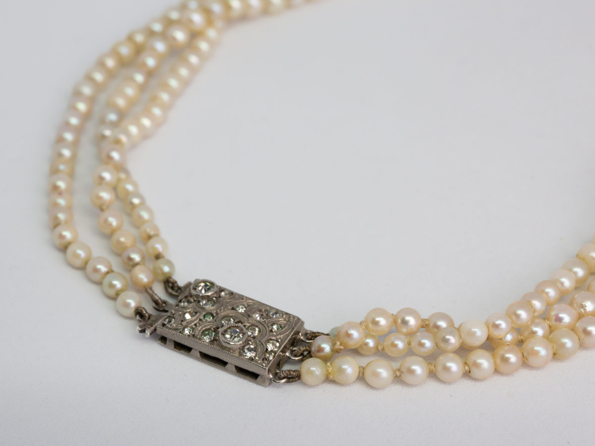 Art Deco graduated pearl necklace. Stunning necklace with 3 strands of graduated pearls and a paste stone encrusted clasp. Unidentifiable hallmark to back of clasp. Made in France. Shell shaped box included but not original. Shortest strand measures approximately 420mm and longest 450mm. Necklace weight 47gms. Close up photo of the clasp.