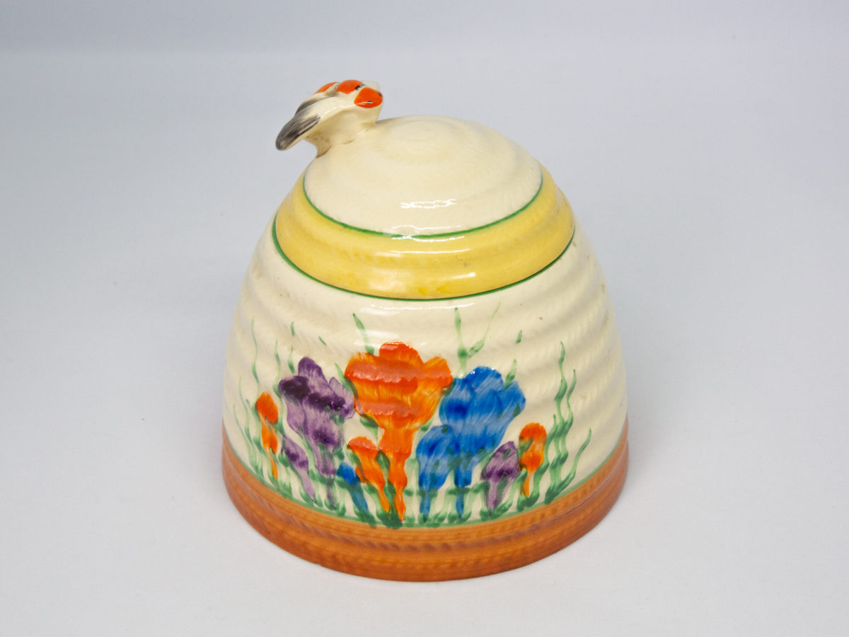 Clarice Cliff 'Autumn Crocus' honey pot. A sweet and classic Clarice Cliff design honey pot hand-painted in the Autumn Crocus pattern. Shaped in the form of a beehive with a bee handle to the lid. In excellent condition throughout with only minor stain on small inside area. Signed Clarice Cliff to the base. c Late 1930s. Base of pot measures 96mm in diameter. Height excluding bee handle 85mm. Photo showing pot with lid in place and bee handle to the left of photo.