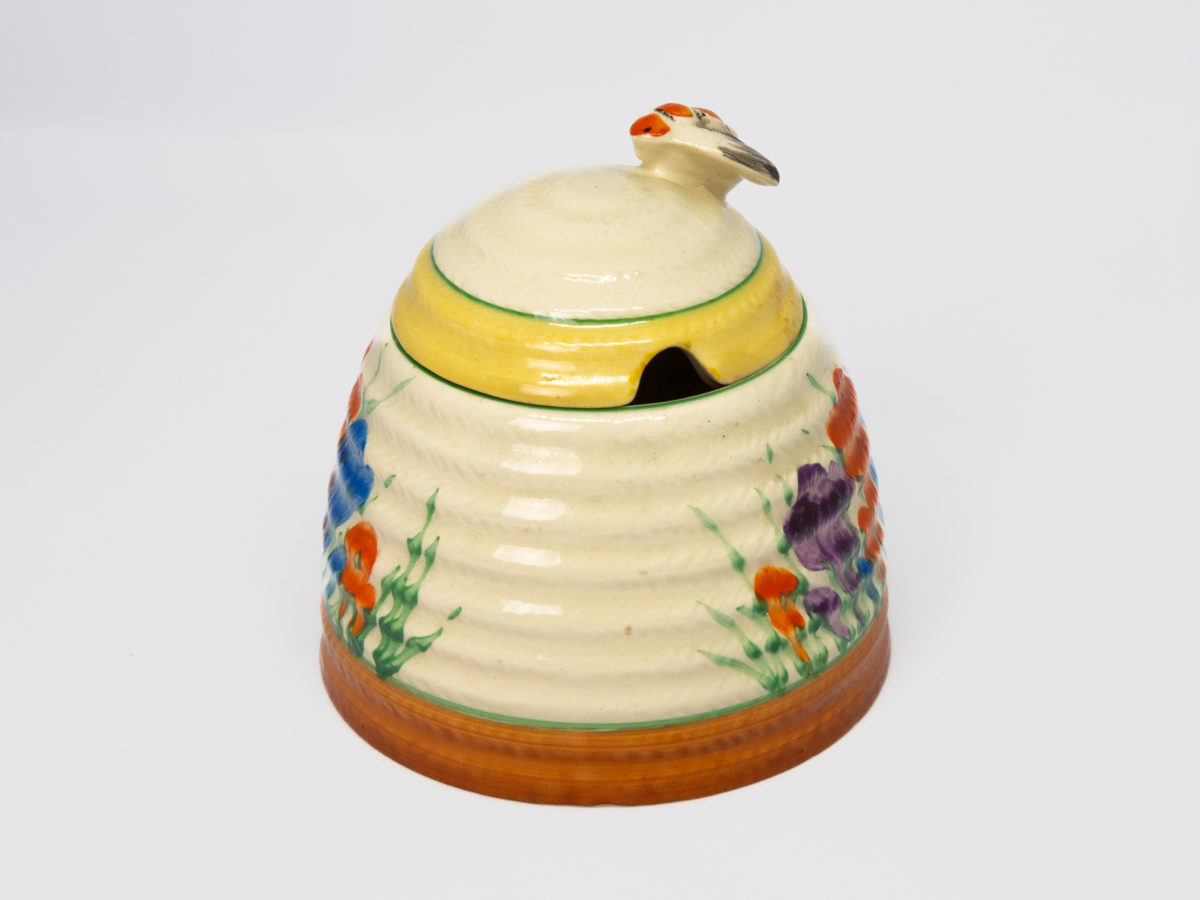 Clarice Cliff 'Autumn Crocus' honey pot. A sweet and classic Clarice Cliff design honey pot hand-painted in the Autumn Crocus pattern. Shaped in the form of a beehive with a bee handle to the lid. In excellent condition throughout with only minor stain on small inside area. Signed Clarice Cliff to the base. c Late 1930s. Base of pot measures 96mm in diameter. Height excluding bee handle 85mm. Photo of pot with lid in place , bee handle to the right, spoon hole in lid visible slightly at right and plain part of pot body to the centre with partial crocus design to both left & right