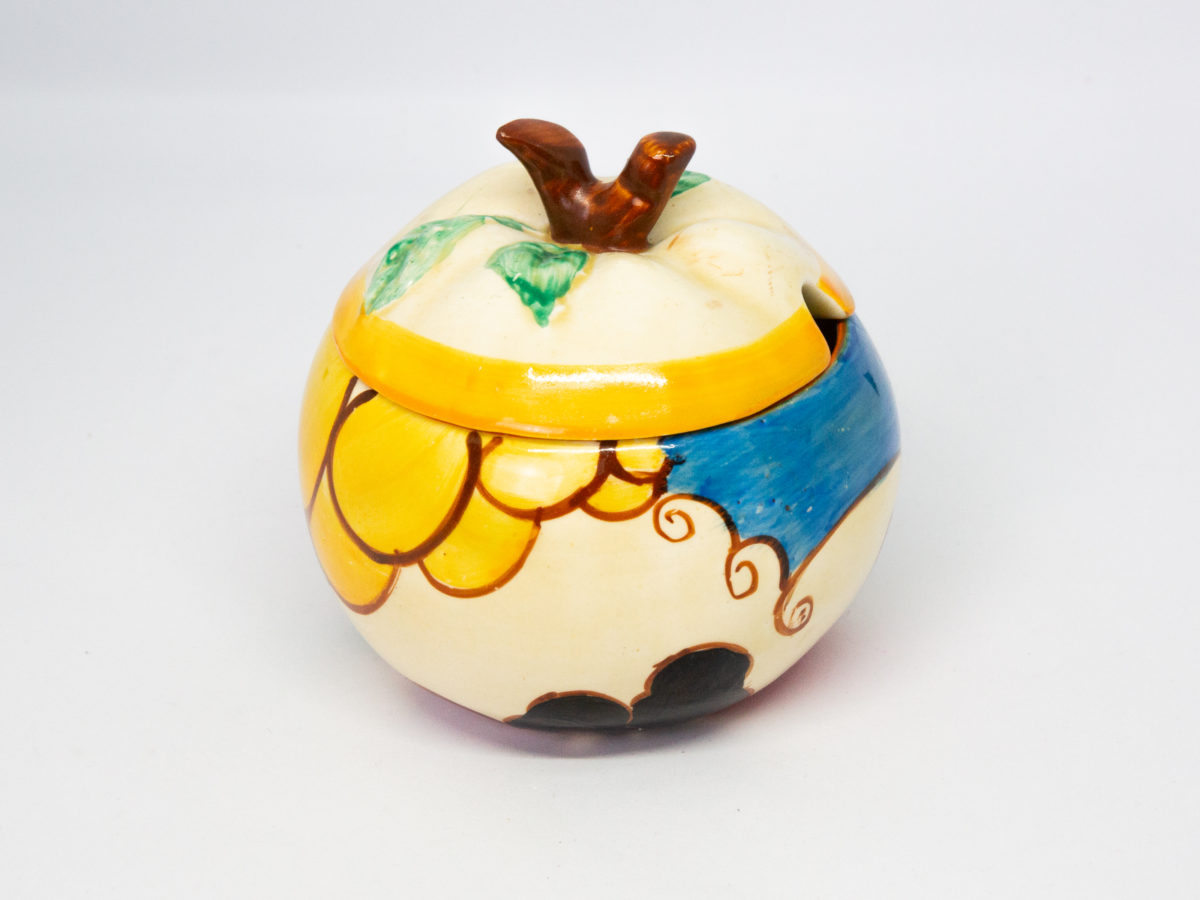 Apple shaped preserve pot by Clarice Cliff. A fun, funky hand-painted preserve pot in the Fantasque Bizarre line, 'Summerhouse' pattern. In excellent condition. Signed to the base. c1931-1933. Measures 50mm in diameter at base, 95mm at bulbous middle and approximately 85mm at tallest. Photo of pot from another angle showing yellow bubble pattern to the left & blue to the right.